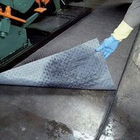 En absorbent matta ligger på marken. En hand håller upp ena änden, visas hur den sugit upp vätska.